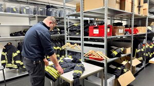 Bild vergr&ouml;&szlig;ern: Ein Mitarbeiter der Berufsfeuerwehr im Kleiderpool mit Einsatzkleidung.