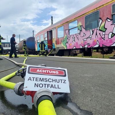 Bild vergr&ouml;&szlig;ern: Verteiler mit einem Schild Achtung Atemschutz Notfall im Hintergrund Einsatzkräfte bei einer Übung.