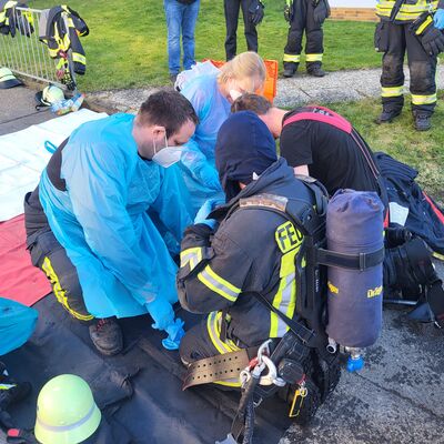 Bild vergr&ouml;&szlig;ern: Einsatzkräfte unter Atemschutz werden nach einem Einsatz von Kollegen ausgekleidet
