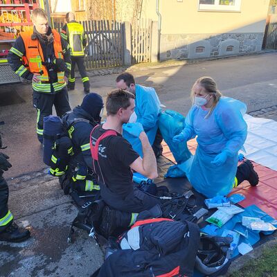 Bild vergr&ouml;&szlig;ern: Einsatzkräfte unter Atemschutz werden nach einem Einsatz von Kollegen ausgekleidet