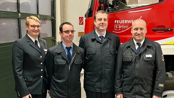 Vier Einsatzkräfte in Uniform vor einem Löschfahrzeug