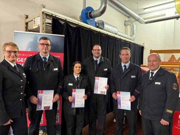 Sechs Einsatzkräfte in Uniform, vier davon mit Beförderungsurkunden