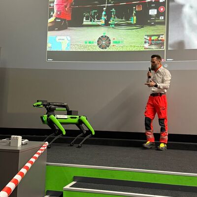 Bild vergr&ouml;&szlig;ern: Person auf einer Bühne vor einer Päsentationsleinwand der einen Roboter vorstellt