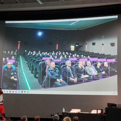 Bild vergr&ouml;&szlig;ern: Personen vor Präsentation auf der eine Menschenerkennung mittels KI gezeigt wird