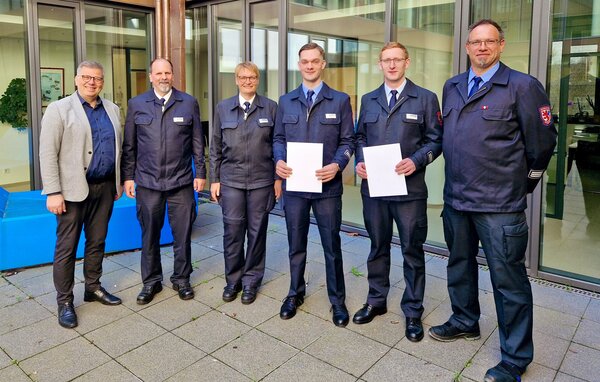 Fünf Einsatzkräfte in Uniform und eine Zivilperson. Zwei der Einsatzkräfte halten eine Beförderungsurkunde in der Hand.