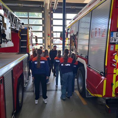 Bild vergr&ouml;&szlig;ern: Mädchen in Jugendfeuerwehrbekleidung zwischen Einsatzfahrzeugen