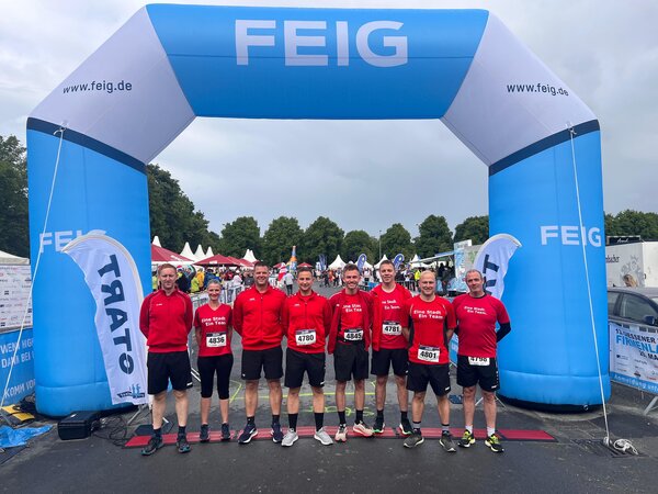 Mehrere Feuerwehrleute in Sportklamotten vor dem Zielbogen des Firmenlaufs.