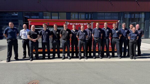 16 Feuerwehr-Einsatzkräfte vor einem Abbrollbehälter
