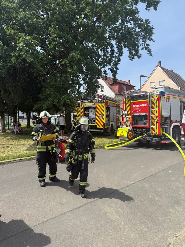 Zwei Feuerwehreinsatzkräfte in Schutzausrüstung, dahinter zwei Löschfahrzeuge