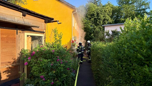 Zwei Einsatzkräfte unter Atemschutz vor Wohngebäude. Im Hintergrund ist Brandrauch zu sehen.