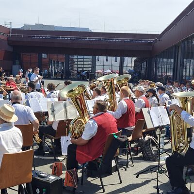Bild vergr&ouml;&szlig;ern: Musikkapelle spielt vor Hallentoren und Zuschauer hören gespannt zu.