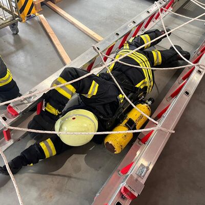 Bild vergr&ouml;&szlig;ern: Einsatzkraft unter Atemschutz rutscht durch ein Leitergerüst, welches mit Leinen verspannt ist
