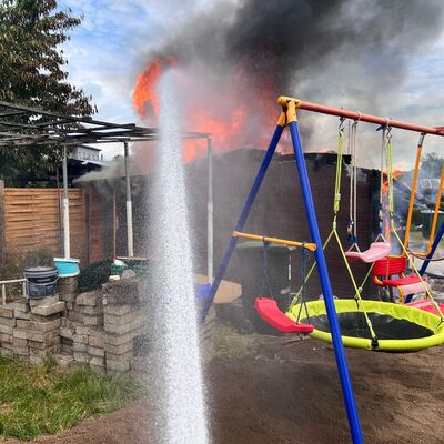 Bild vergr&ouml;&szlig;ern: Spielgeräte von Kindern und ein Wasserstrahl im Vordergrund, dahinter starker Flammenschein