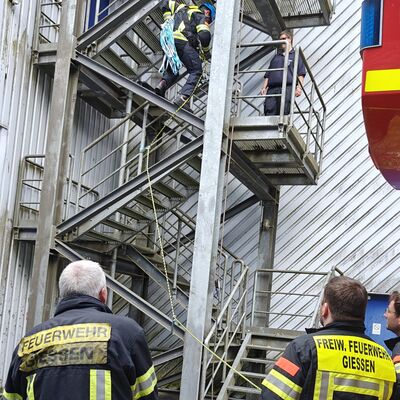 Bild vergr&ouml;&szlig;ern: Zwei Einsatzkräfte im Vordergrund sichern mit einem Seil eine Einsatzkraft am Gerüst im Hintergrund.