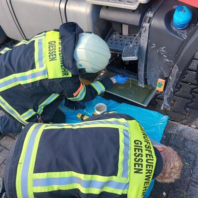 Bild vergr&ouml;&szlig;ern: Zwei Einsatzkräfte knieen vor einem LKW mit einem aufgerissenen Dieseltank. Unter dem Dieseltank steht eine Wanne zum Auffangen des Kraftstoffes.