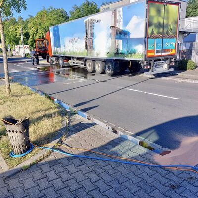 Bild vergr&ouml;&szlig;ern: Auf einer Straße steht ein LKW, aus dem Kraftstoff austritt und über eine Straße läuft. Im Vordergrund ist ein Kanaleinlauf zu sehen, der mit Ölbindemittel eingedeicht wurde.