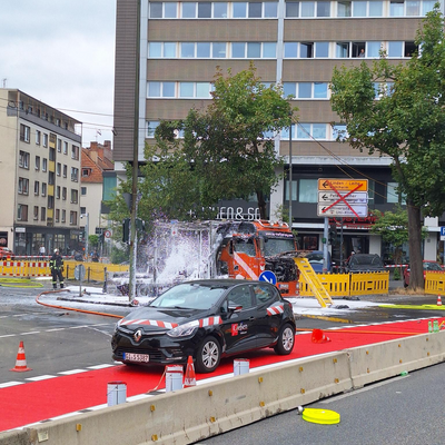 Bild vergr&ouml;&szlig;ern: Ausgebrannter LKW überzogen mit Löschschaum, vor einem Gebäude.