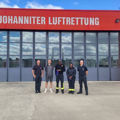 Bild vergr&ouml;&szlig;ern: Fünf Personen vor einem Hubschrauber-Hangar