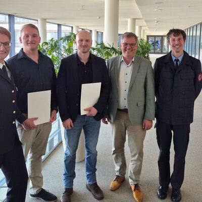 Bild vergr&ouml;&szlig;ern: Mehrere Personen in einem Flur, zwei haben eine Urkunde in der Hand.