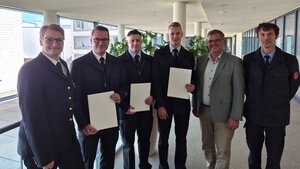 Mehrere Personen in einem Flur, drei halten eine Urkunde in der Hand.